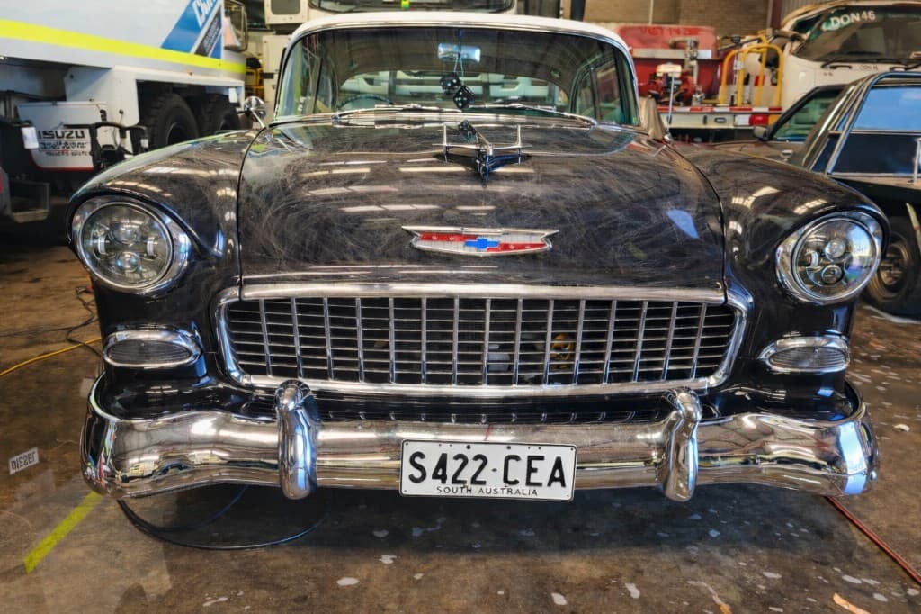 Classic Chevrolet front with severe swirl marks and hazy black paint before correction